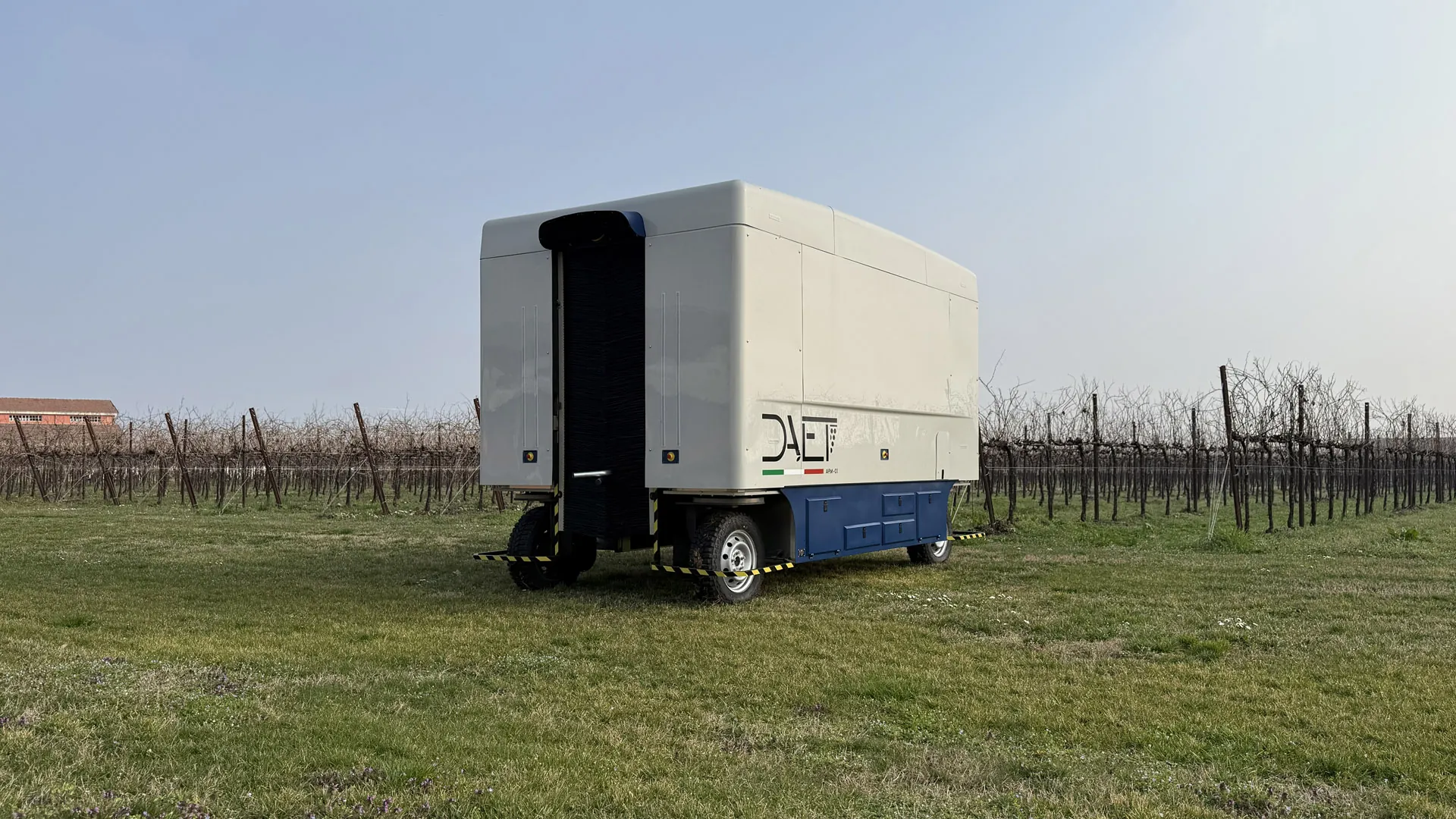 Three-quarter view of the autonomous winter vine pruning machine A.P.M.-01 next to a pruned row